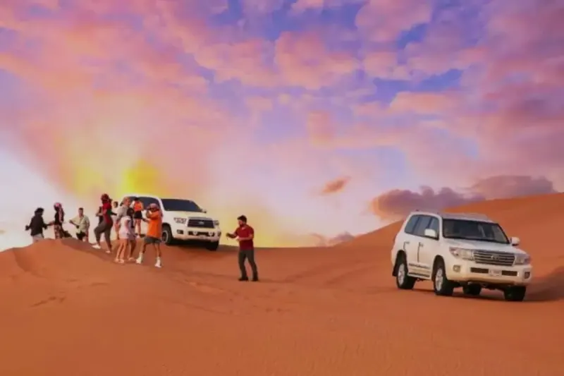 Guests enjoying the sunset next to Land Cruisers on a Buy 1 Get 1 Free desert safari in Dubai
