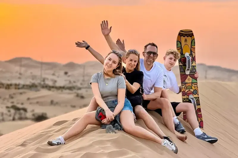 Family with a sandboard on top of a dune during a half day desert safari in Dubai
