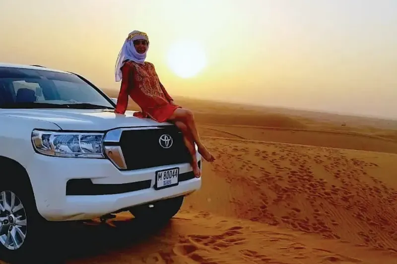Guest sitting on a Land Cruiser as the sun rises over the Dubai desert