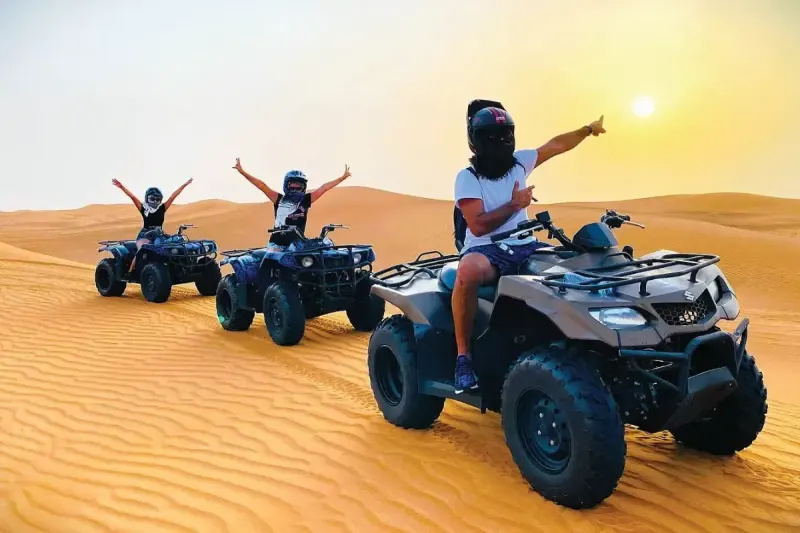 Riders on ATV quad bikes in the Dubai desert at sunset